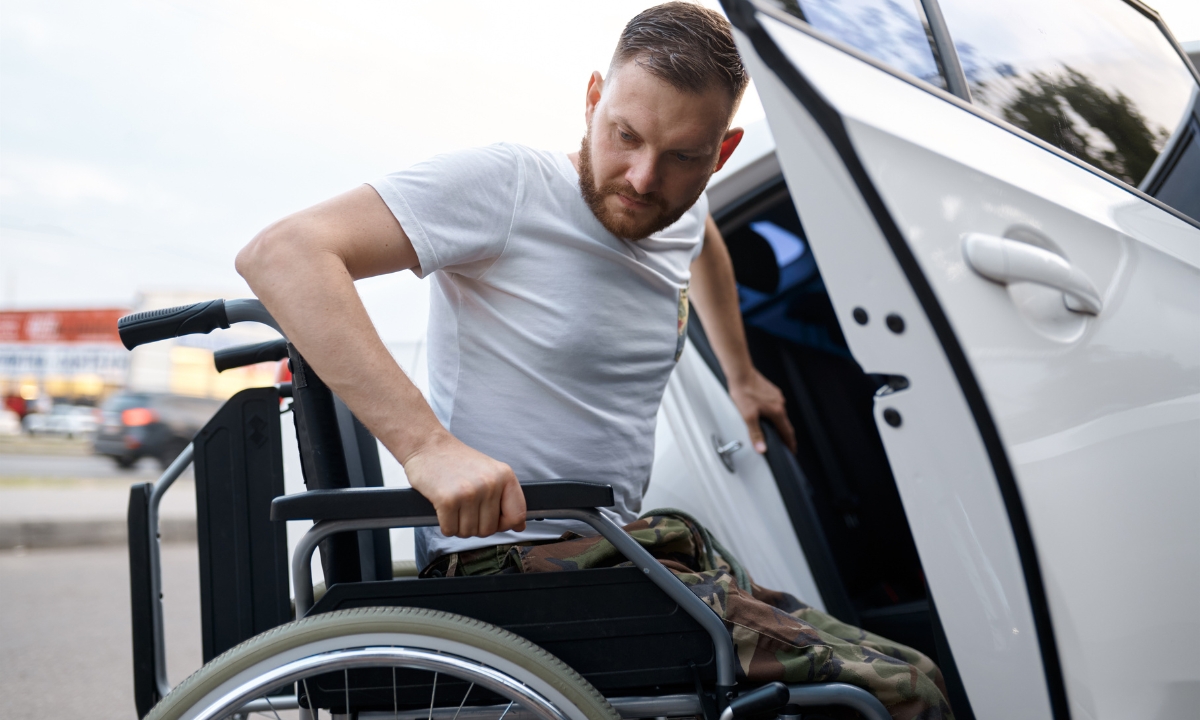 a man in camo pants getting out of a wheelchair and into a car