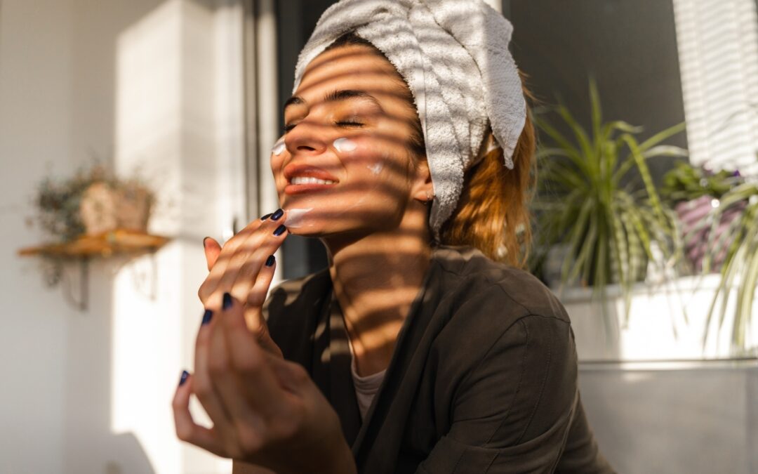a woman with a towel on her head spreading moisturizer on her face