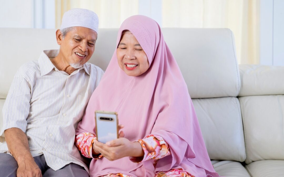 a senior couple sitting on a couch smiling at a phone