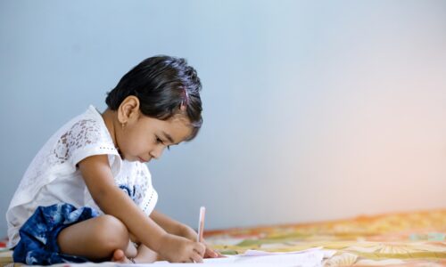 a small child drawing on a piece of paper on the floor