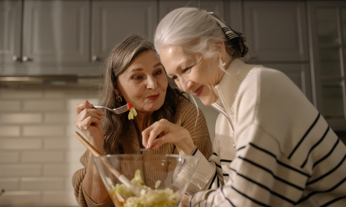 two elderly women eating a salad straight from a salad bowl