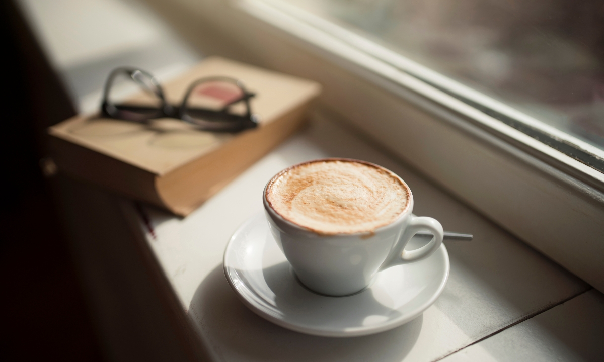 a book, pair of glasses, and cup of coffee on a windowsill