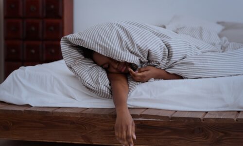 a sleeping person tangled in a blanket with their arm hanging off the side of the bed