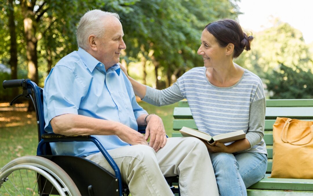 a middle aged woman sitting on a bench next to her wheelchair-bound father