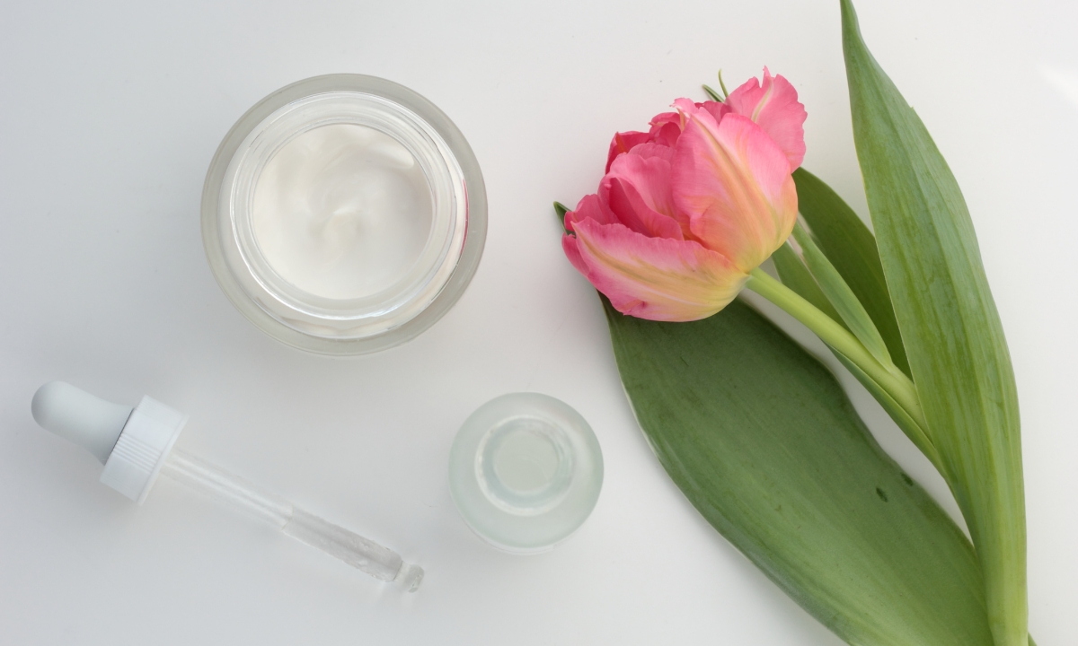 two pots of self-care products, a dropper of serum, and a tulip