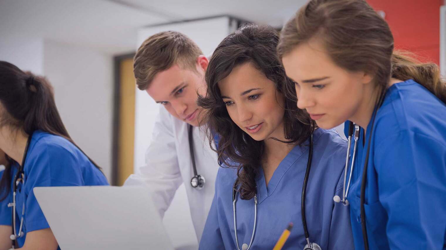 a group of nurses and doctors standing around a laptop