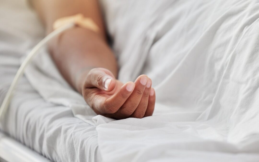 a person's hand on a hospital bed, there is an IV in their arm