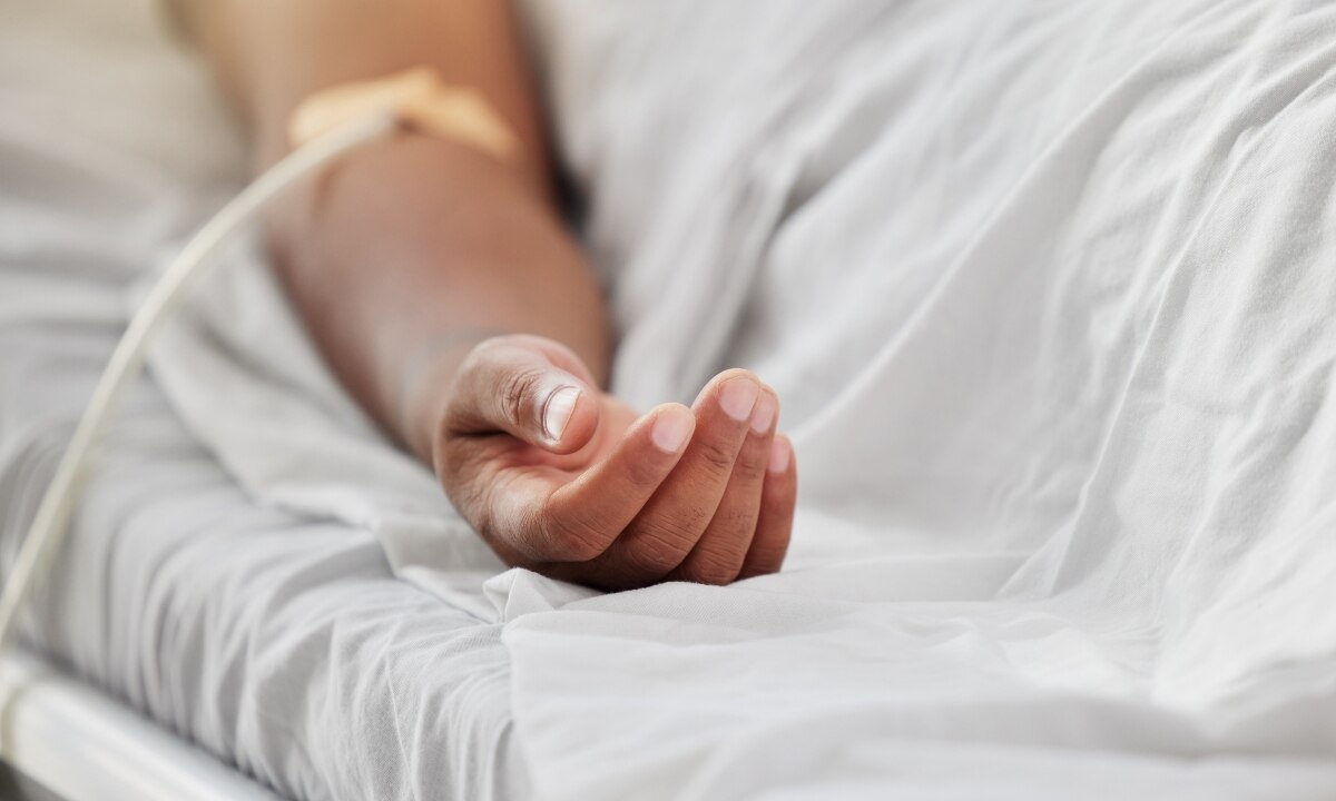 a person's hand on a hospital bed, there is an IV in their arm