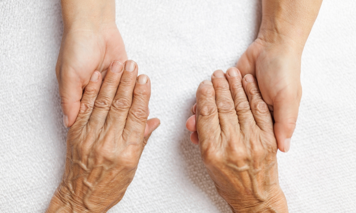 two pairs of hands, one wrinkled and aged, the other younger; they're holding each other gently