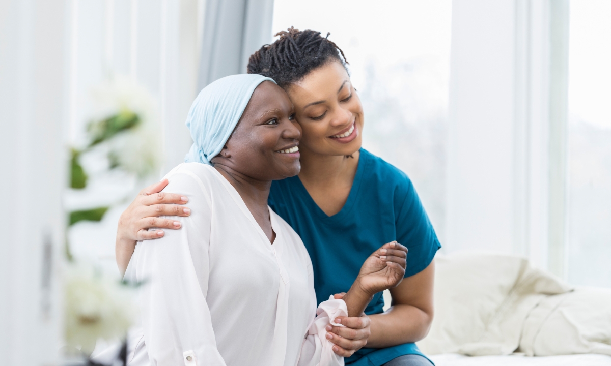 an in-home nurse hugging a cancer patient with a wrap on their head