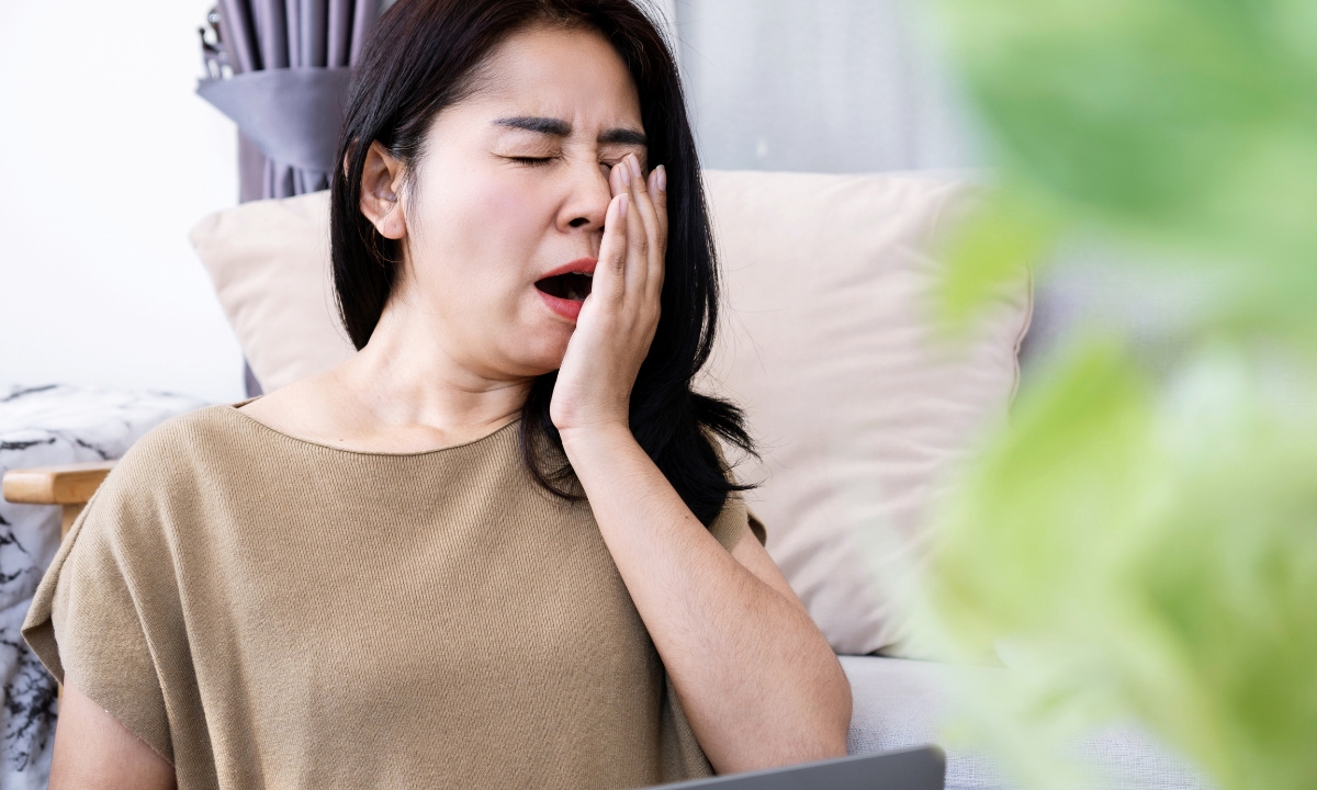 a woman seated on her couch, yawning into her hand