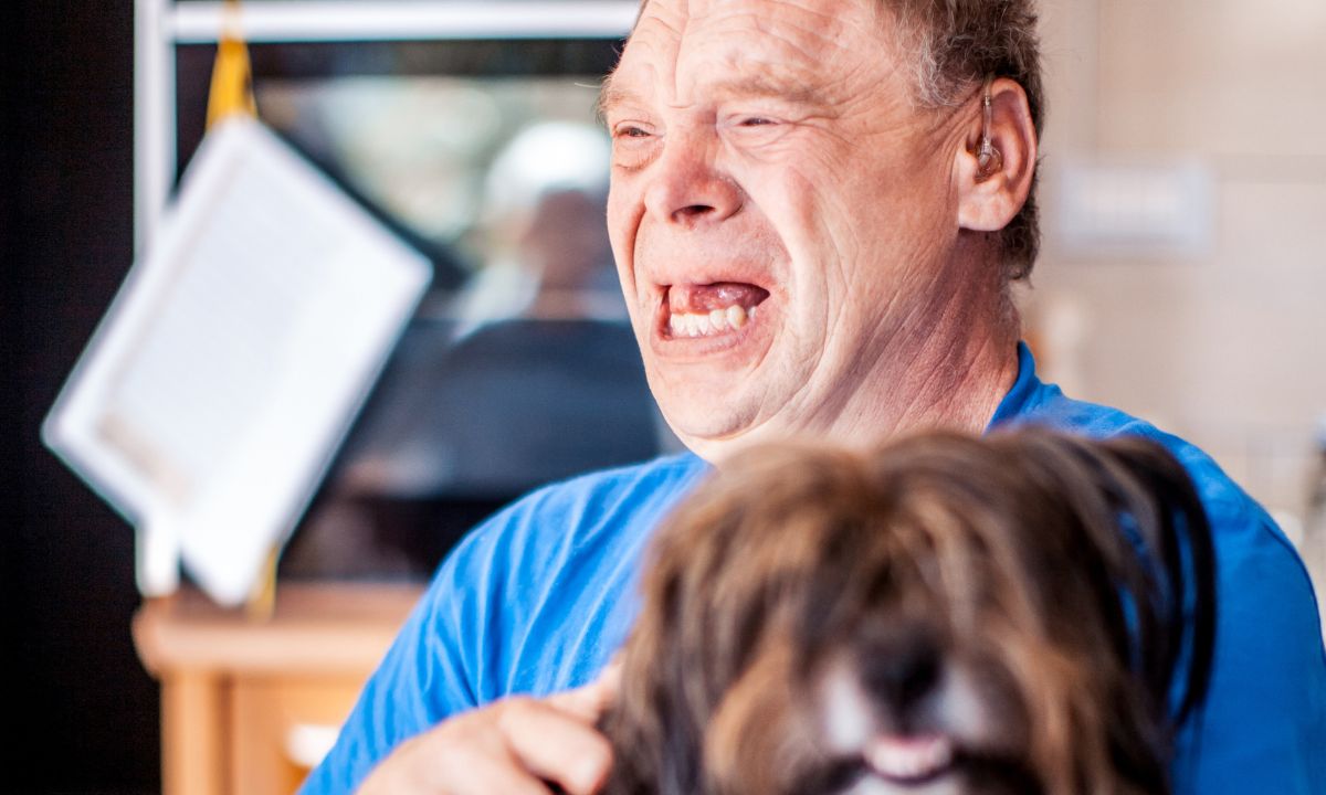 a senior man with Down syndrome smiling and crying while holding a dog