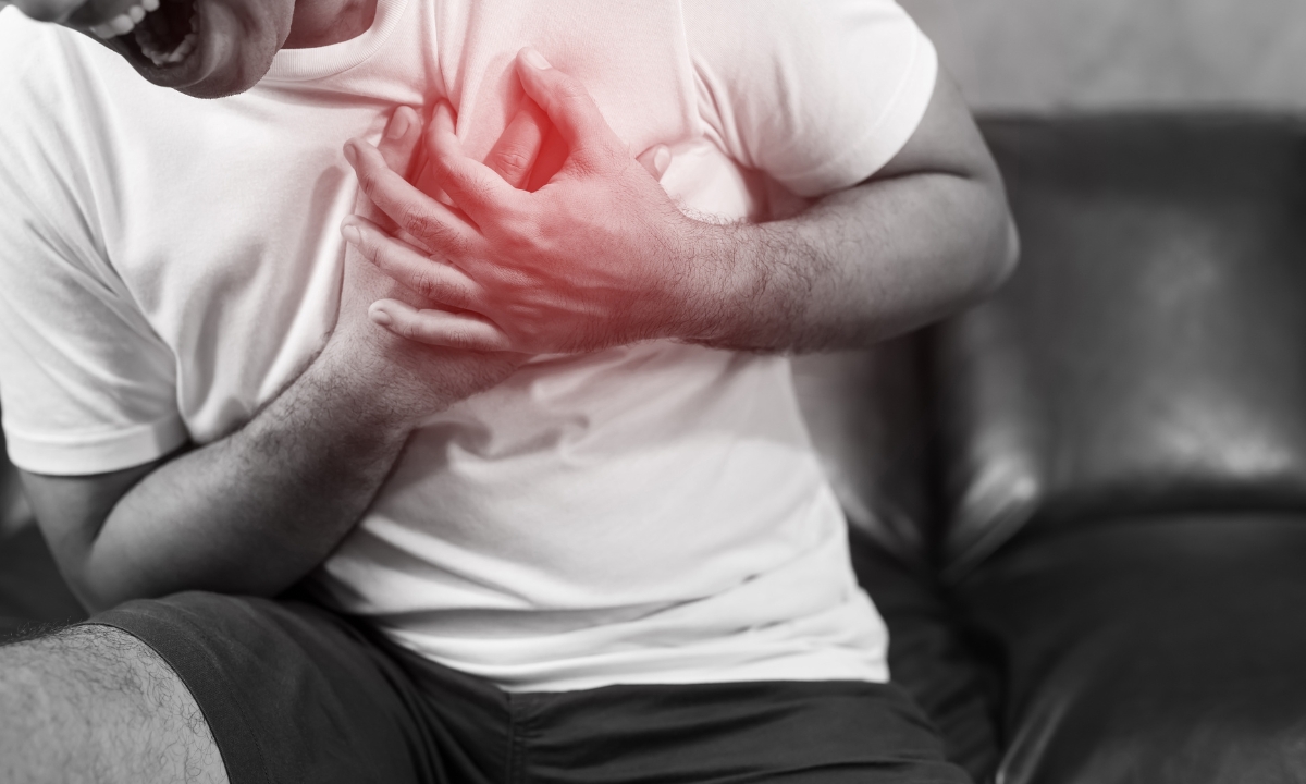 a person with their hands over their heart doubled over in pain: the photo is in black and white and there's an opaque red spot over the heart