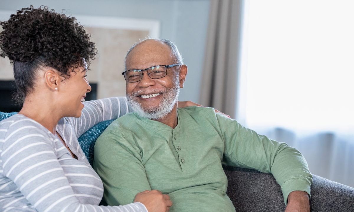 a senior and his daughter on a couch, smiling at each other