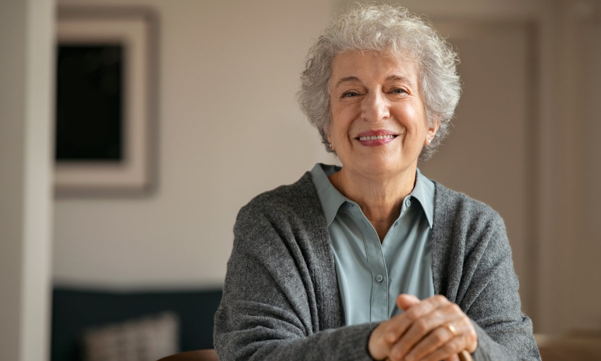 a senior lady smiling for the camera with her hands resting on her cane