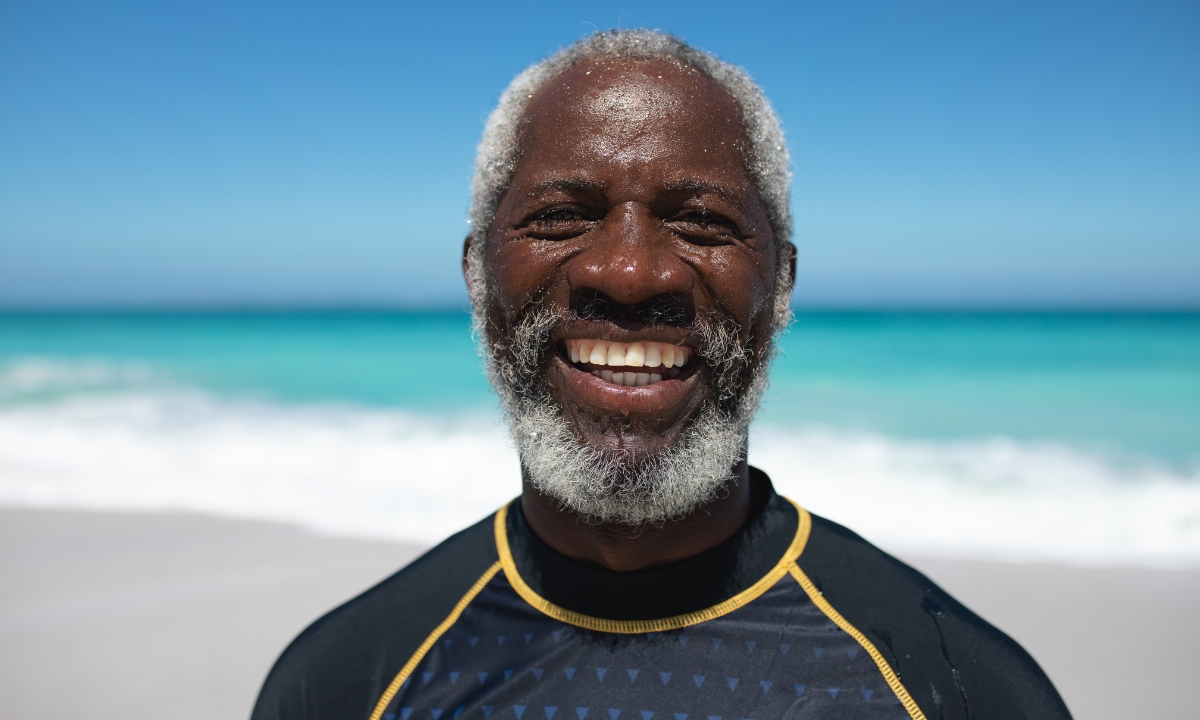 a smiling elderly man on the beach, wearing a wetsuit 