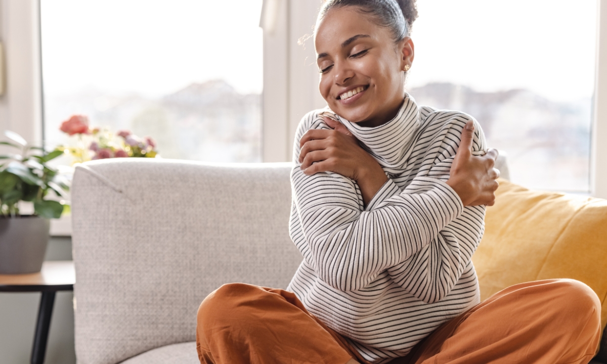 a woman in a cozy sweater smiling and hugging herself