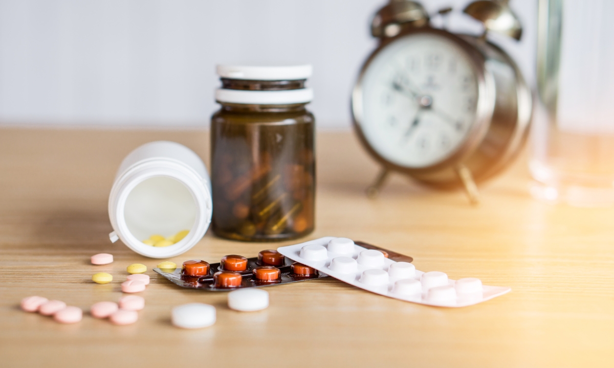 a collection of pills and medications by an old-fashioned alarm clock