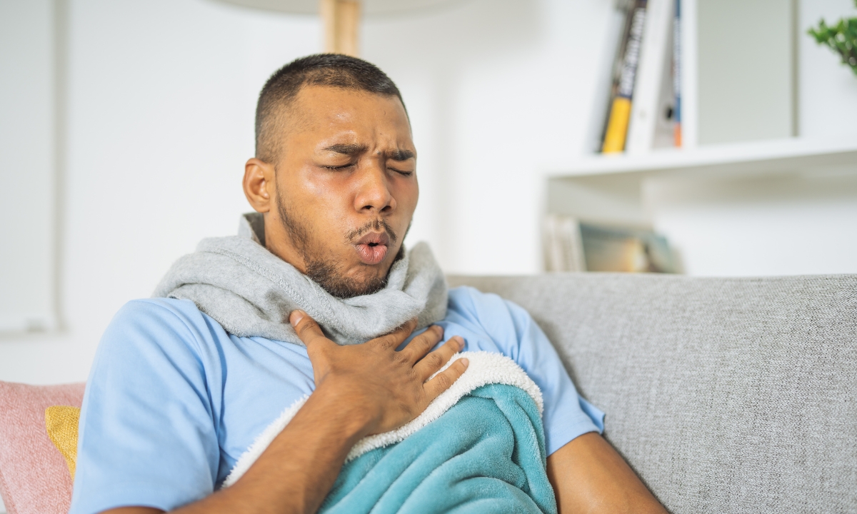 a man under a blanket with his face scrunched up and a hand on his chest