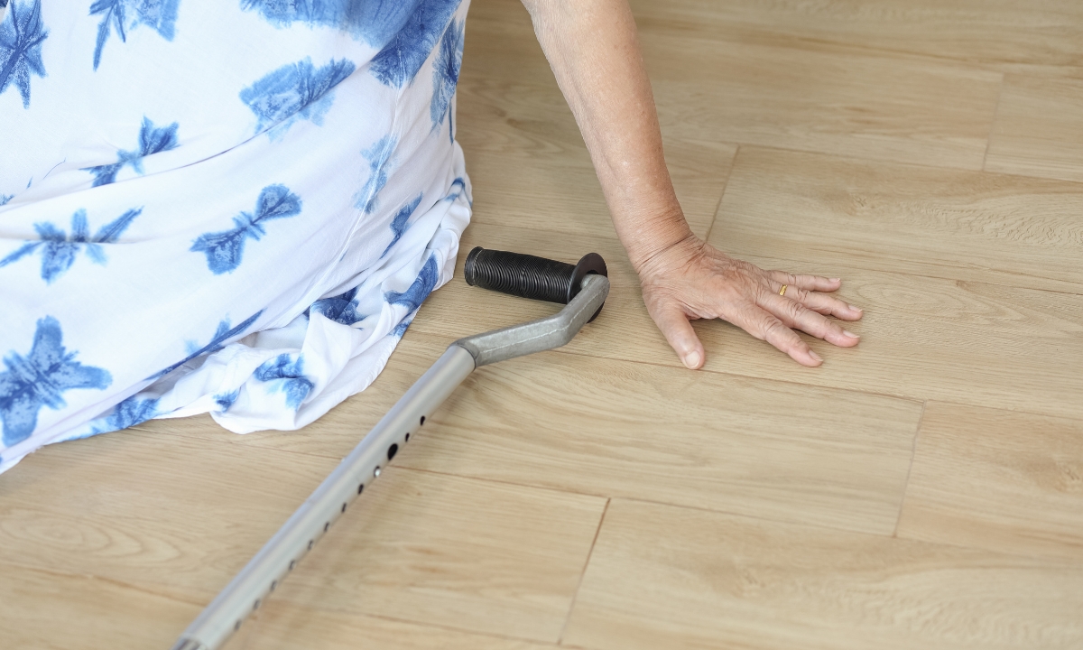 a senior's hand on hardwood flooring beside a cane