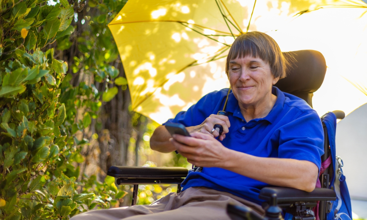 a person with ms in a wheelchair with a phone in one hand and an umbrella in the other