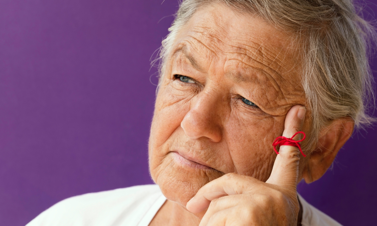 an elderly person with a thoughtful expression and a red string tied to their finger