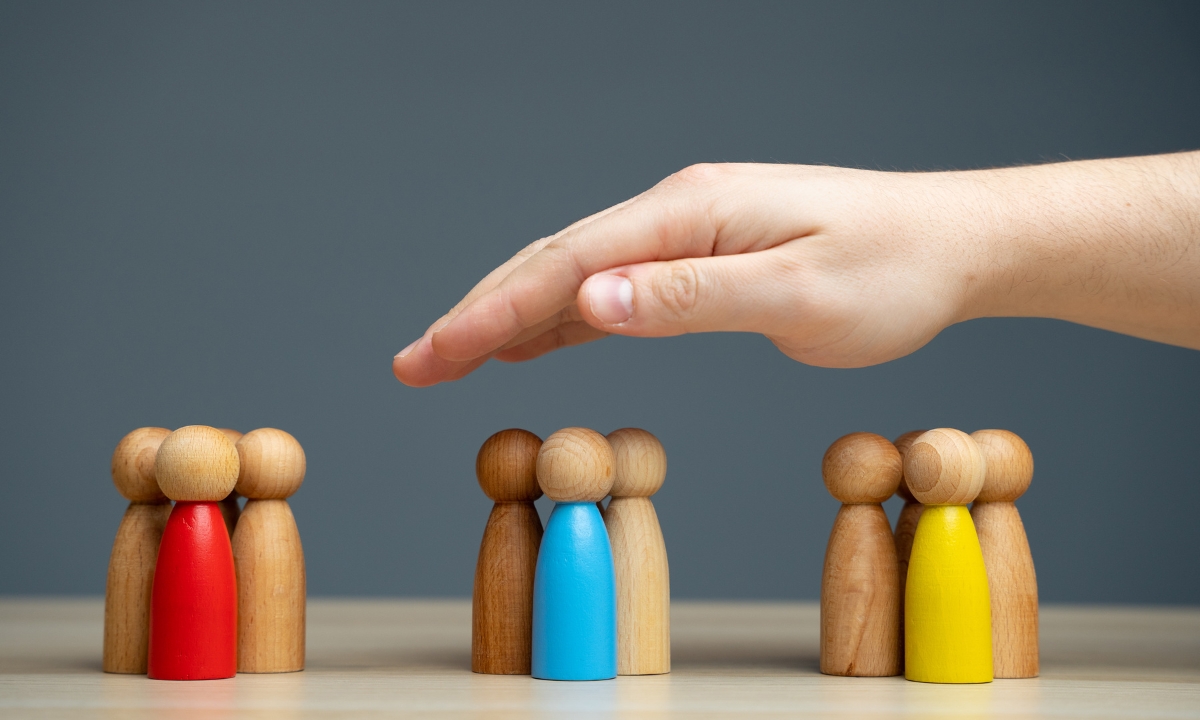 three clusters of four wooden humanoid figurines. each cluster has one figurine painted a primary color. a hand sits in the air above the clusters.