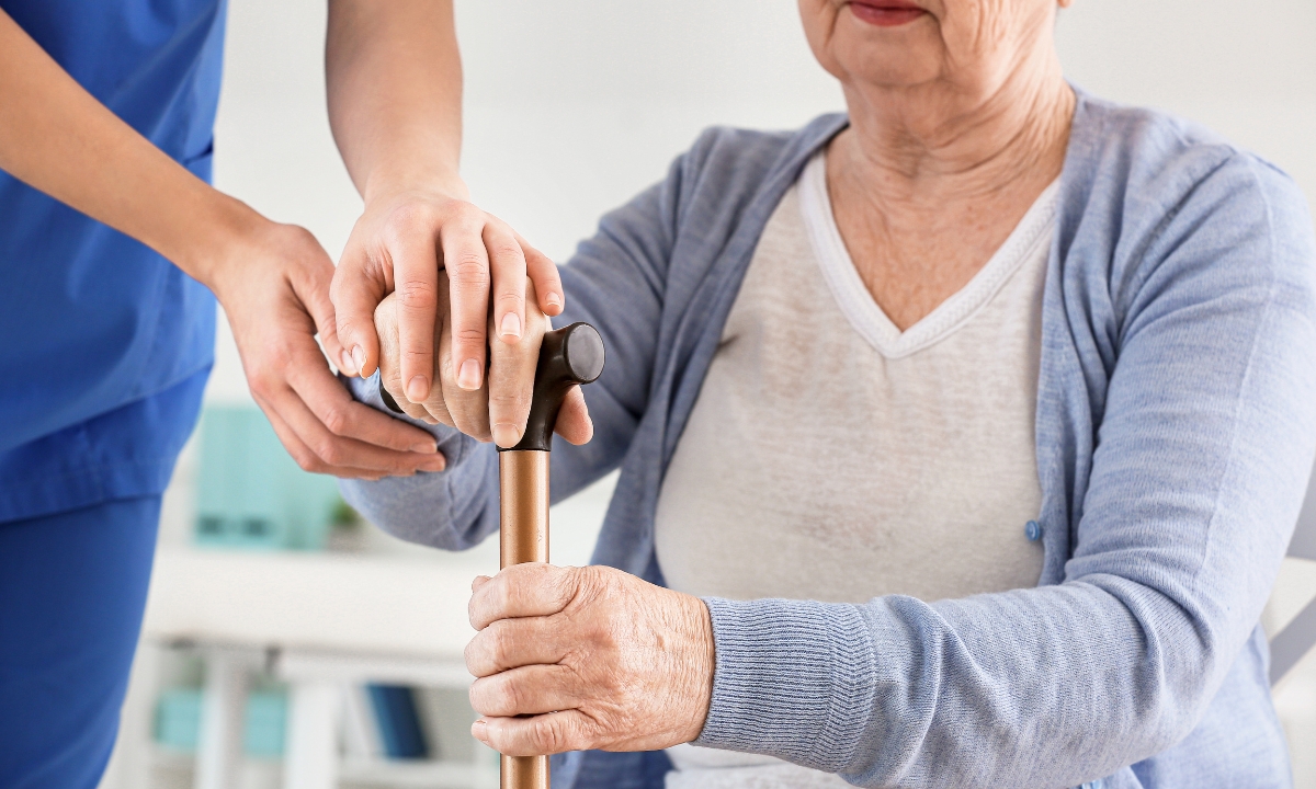 a senior holding a cane and a nurse helping to hold the cane