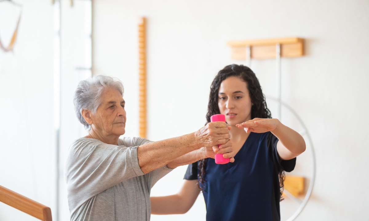 a nurse helping a senior woman lift a small weight for physical therapy