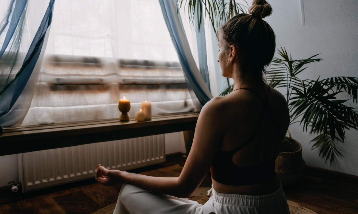 a woman in front of a window and some candles meditating